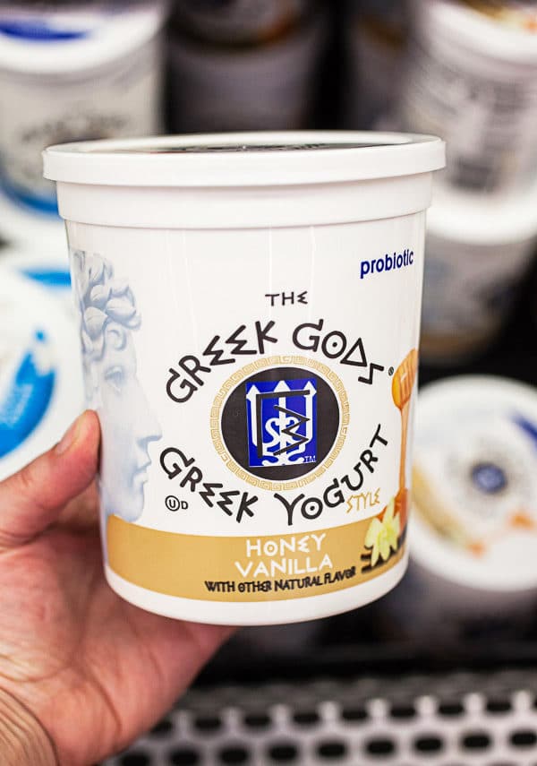 Hand holding plastic tub of Greek Gods yogurt in store.