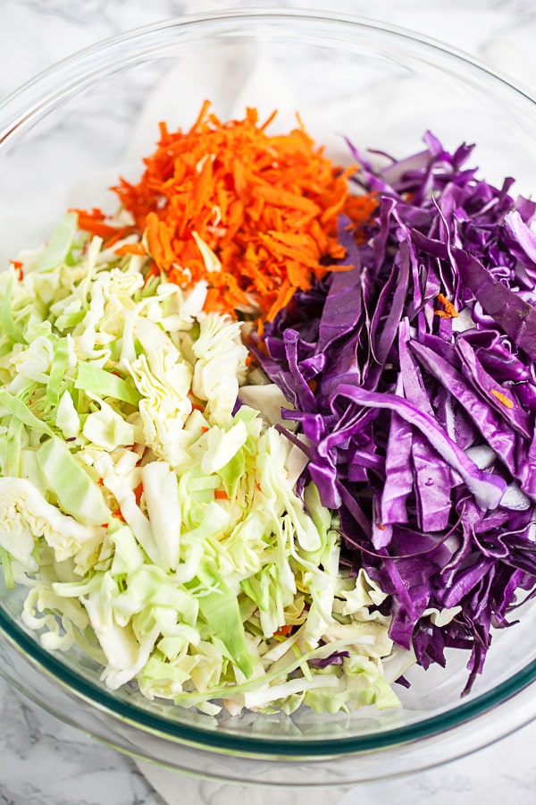 Shredded red and green cabbage and carrots in large glass mixing bowl.