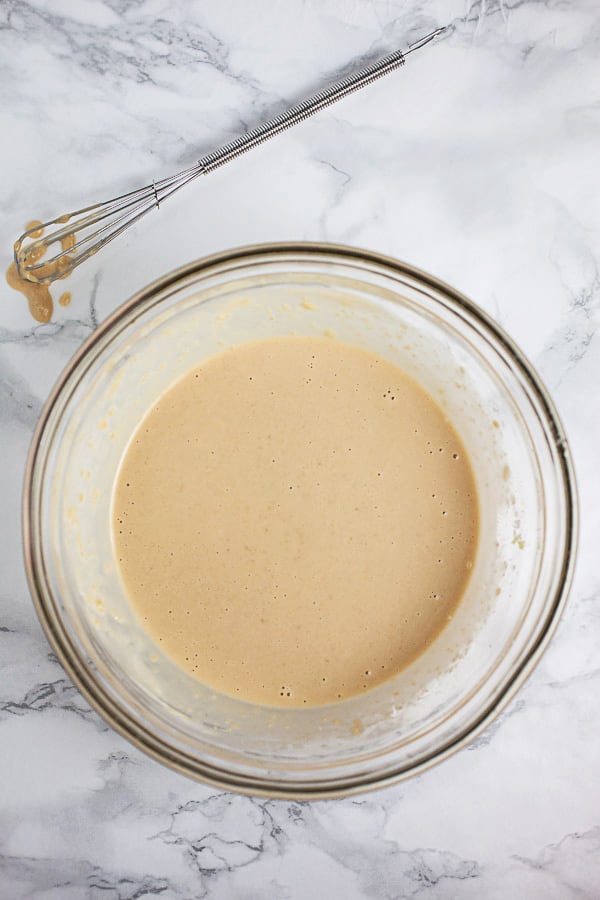 Miso ginger dressing in small glass bowl next to whisk.