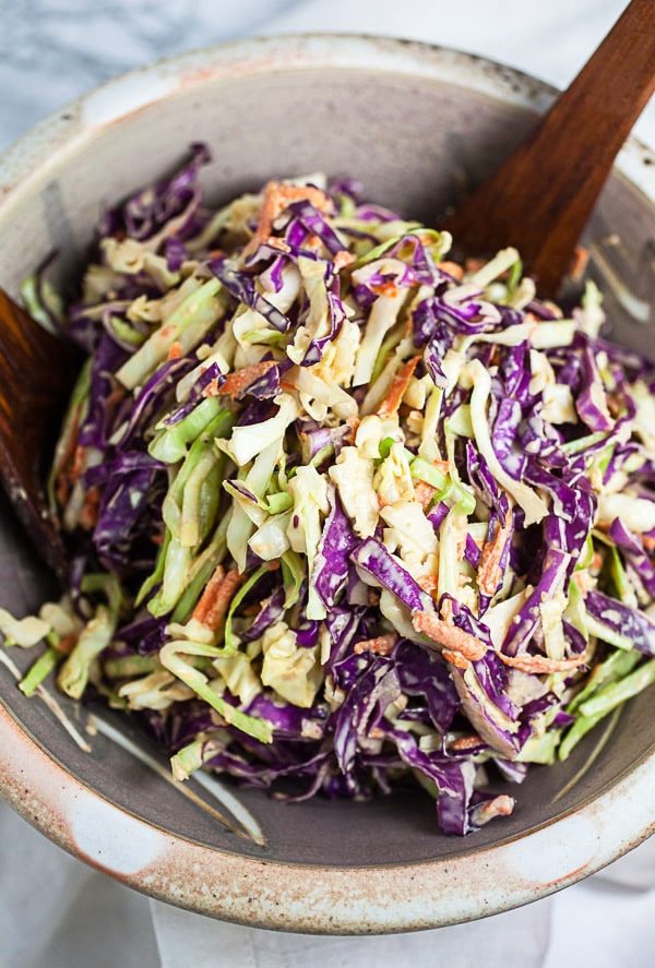 Asian cabbage slaw in ceramic bowl with wooden serving spoons.