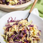 Red and green Asian cabbage slaw in white bowl with fork.
