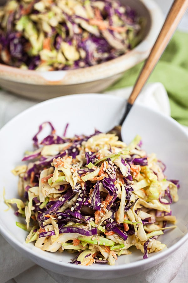 Red and green Asian cabbage slaw in white bowl with fork.