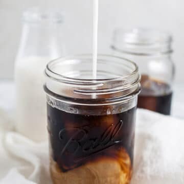 Almond milk poured into mason jar of cold brew coffee.