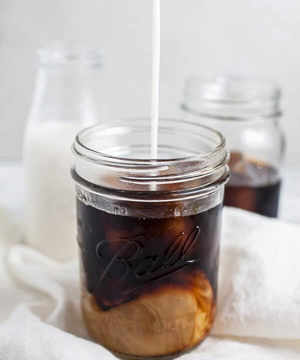Almond milk poured into mason jar of cold brew coffee.