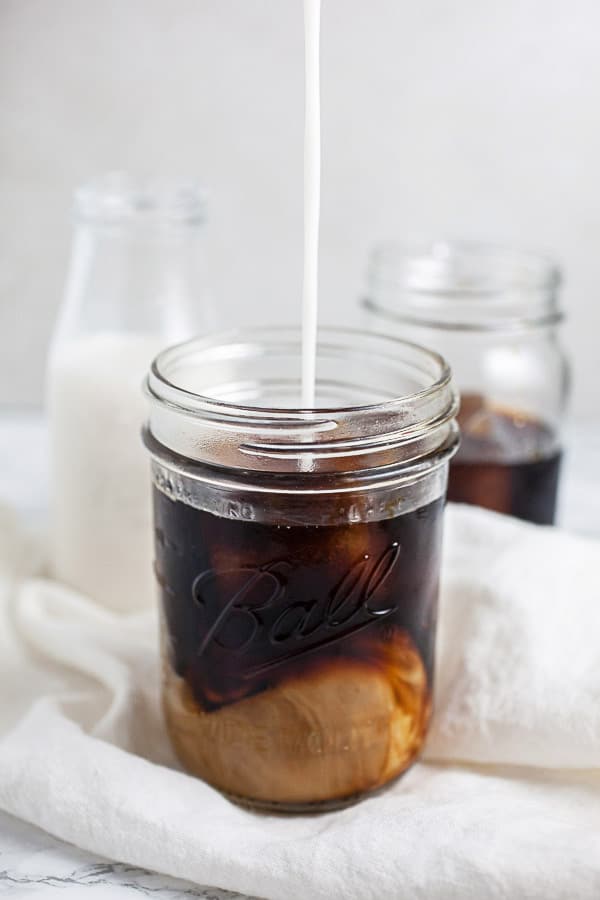 Almond milk poured into mason jar of cold brew coffee.