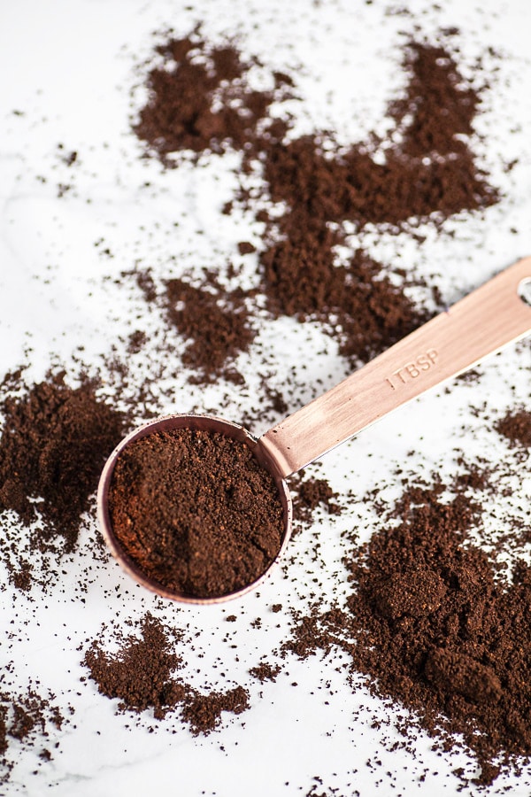 Coffee grounds spilling out of tablespoon on white surface.