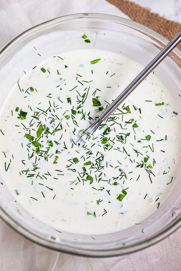 Creamy dressing topped with minced herbs in small glass bowl with whisk.