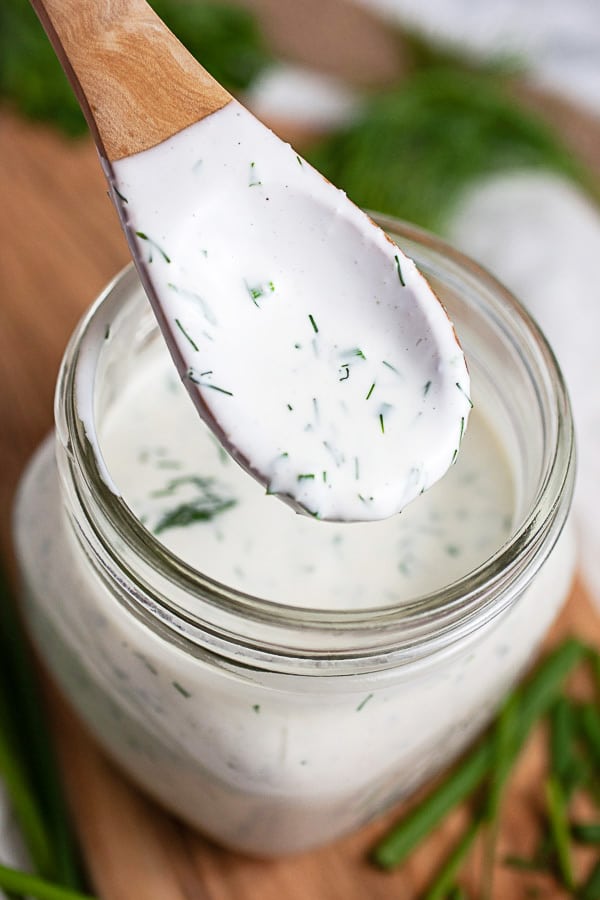 Spoonful of homemade ranch dressing lifted from glass jar.