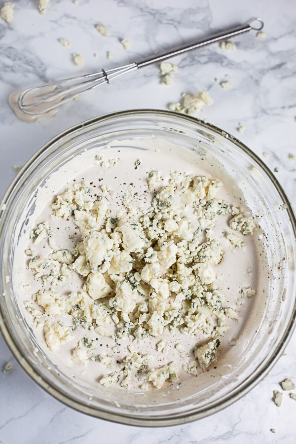 Creamy dressing with blue cheese crumbles in small glass bowl.