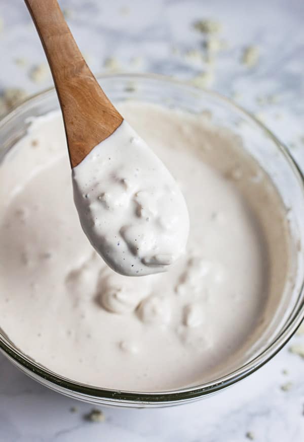 Spoonful of blue cheese dressing lifted from small glass bowl.