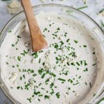 Homemade blue cheese dressing with minced chives in small glass bowl with wooden spoon.
