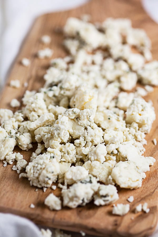 Blue cheese crumbles on small wooden serving board.