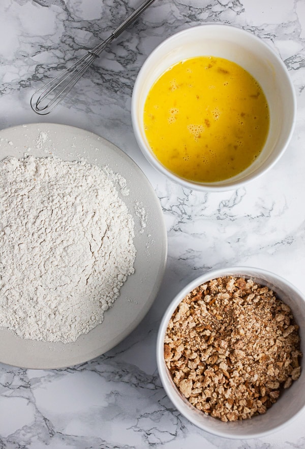 Flour, Panko breadcrumbs, and beaten eggs in three separate white bowls.