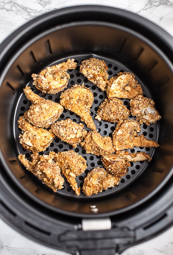 Cooked breaded mushrooms in air fryer basket.