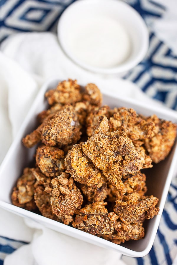 Air fryer breaded mushrooms in white serving platter next to small bowl of ranch dressing.