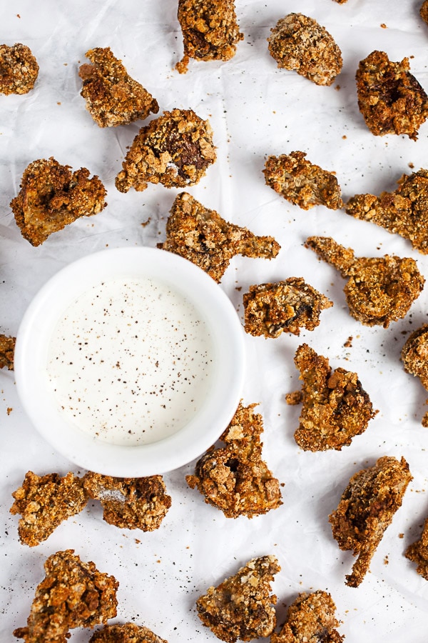 Crispy breaded mushrooms on white surface next to small bowl of ranch dressing.