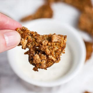 Fingers holding crispy air fryer breaded mushroom in front of small bowl of ranch dressing.