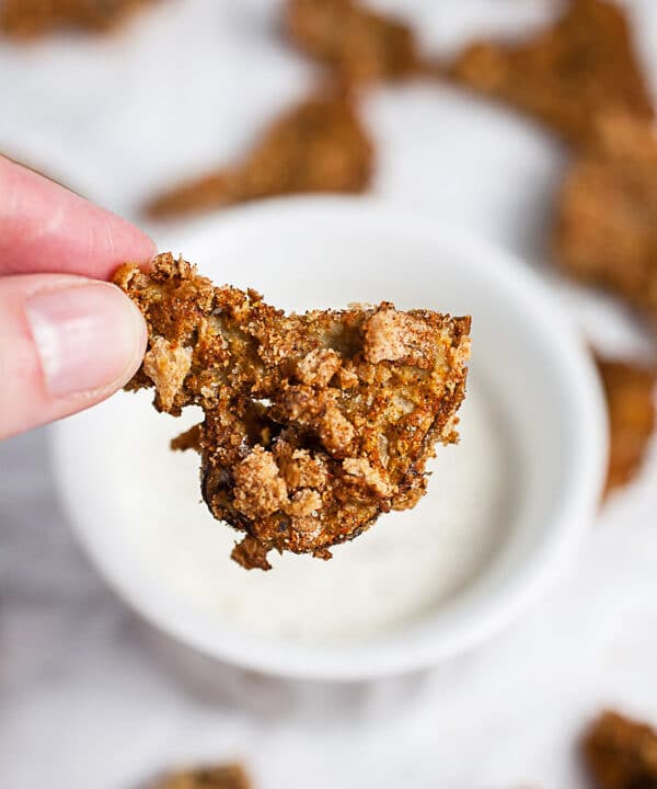 Fingers holding crispy air fryer breaded mushroom in front of small bowl of ranch dressing.