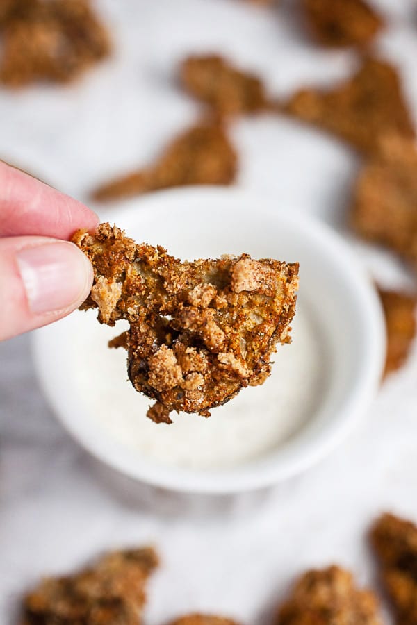 Fingers holding crispy air fryer breaded mushroom in front of small bowl of ranch dressing.