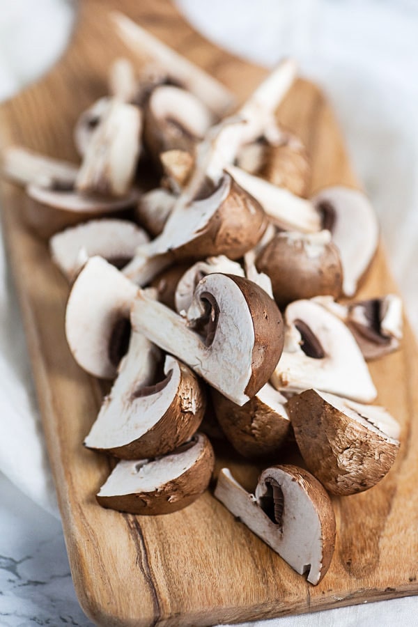 Sliced Baby Bella mushrooms on small wooden serving board.