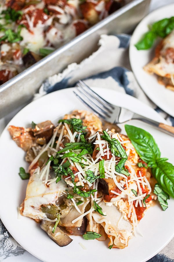 Garden vegetable lasagna with Parmesan cheese and fresh basil on small white plates.