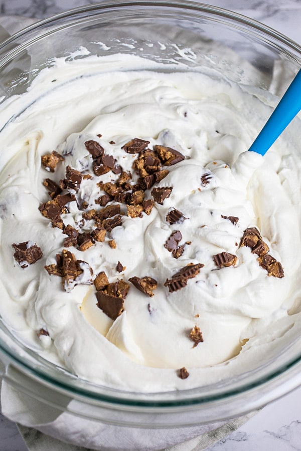 Chopped Reese's Peanut Butter Cups added to cream mixture in glass mixing bowl.