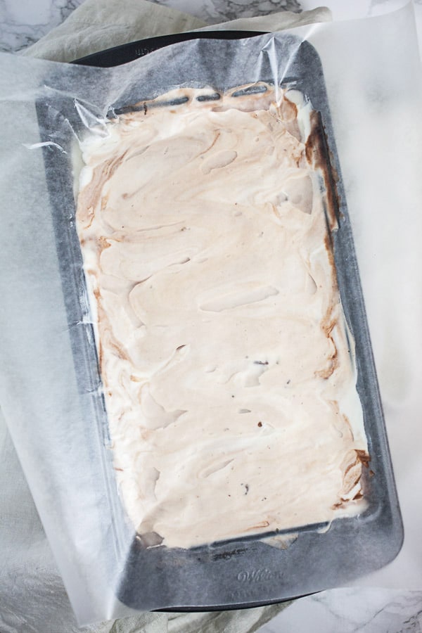 Unfrozen ice cream mixture in metal bread pan topped with wax paper.