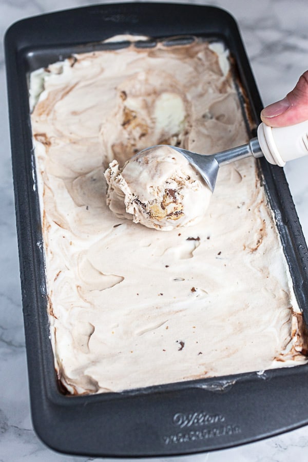 Hand scooping frozen ice cream from metal bread pan.