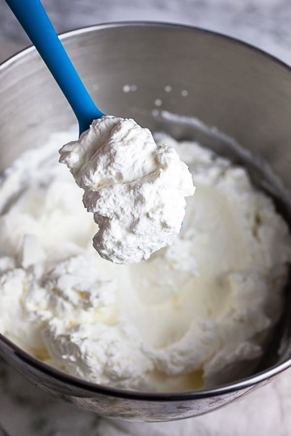 Scoop of whipped cream lifted from metal bowl with blue spatula.
