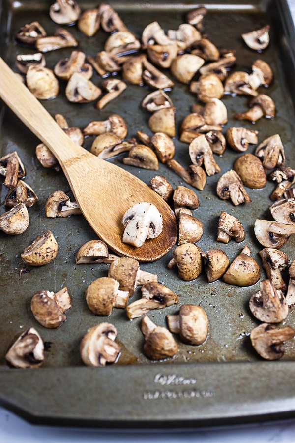 Roasted cremini mushrooms on metal baking sheet with wooden spoon.