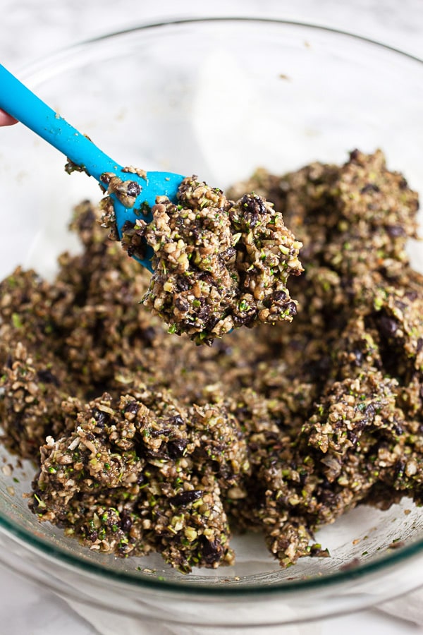 Scoop of veggie burger mixture lifted from glass bowl with blue spatula.