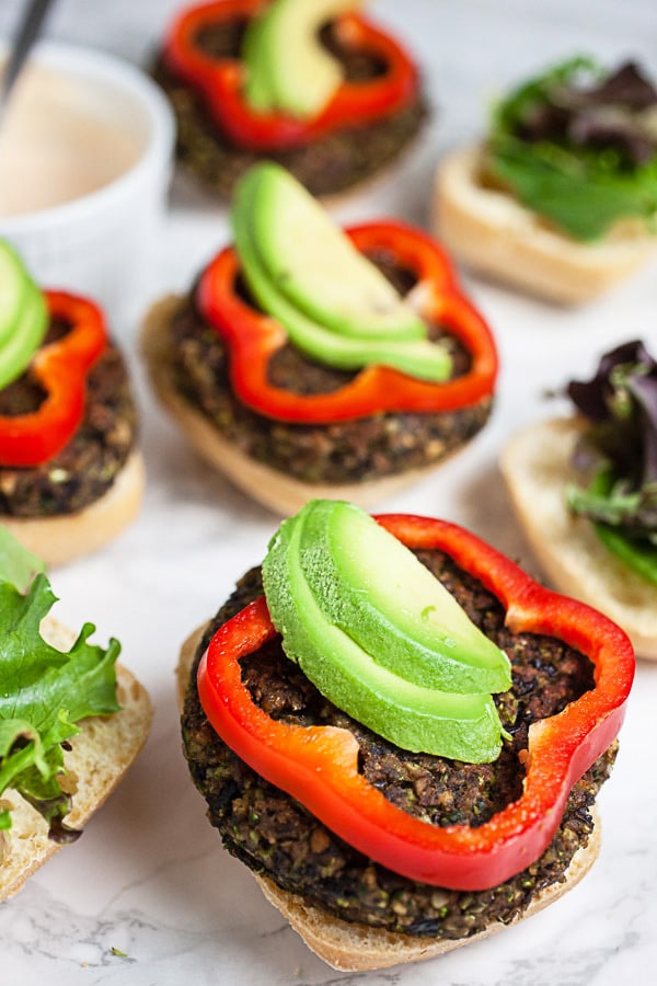 Open faced black bean mushroom burgers with red bell pepper rounds and sliced avocado.
