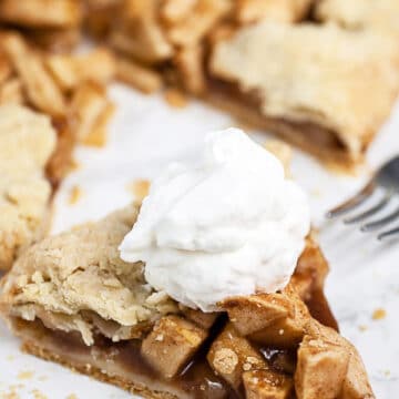 Piece of apple galette with whipped cream on white surface.