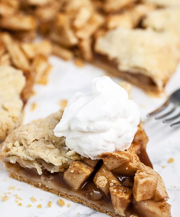 Piece of apple galette with whipped cream on white surface.