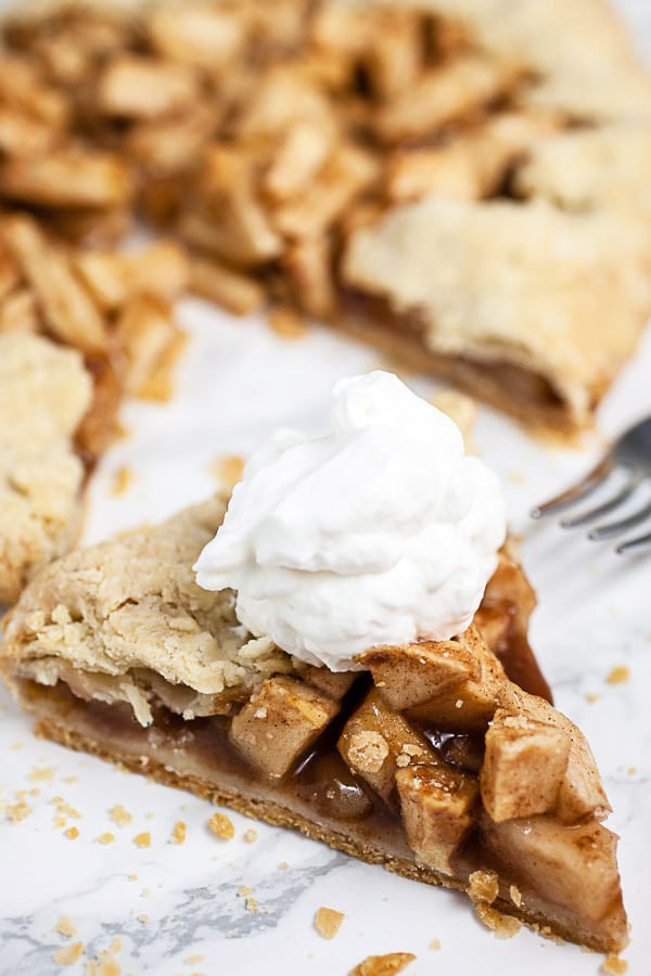 Piece of apple galette with whipped cream on white surface.