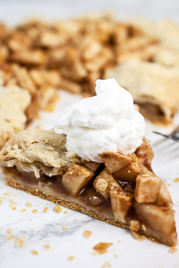 Slice of apple galette with whipped cream on white suface.