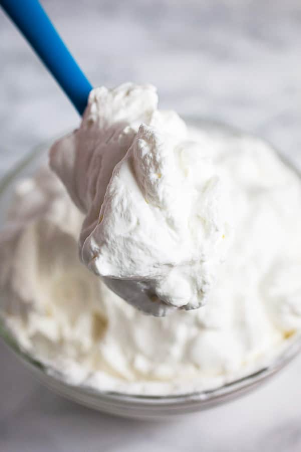 Scoop of whipped cream lifted from glass bowl on blue spatula.