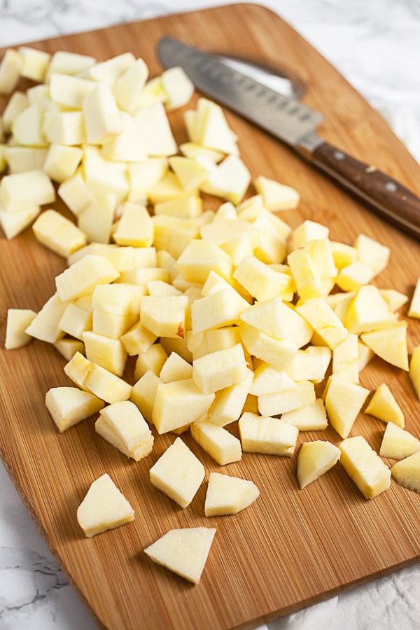 Peeled and diced apples on wooden cutting board with knife.