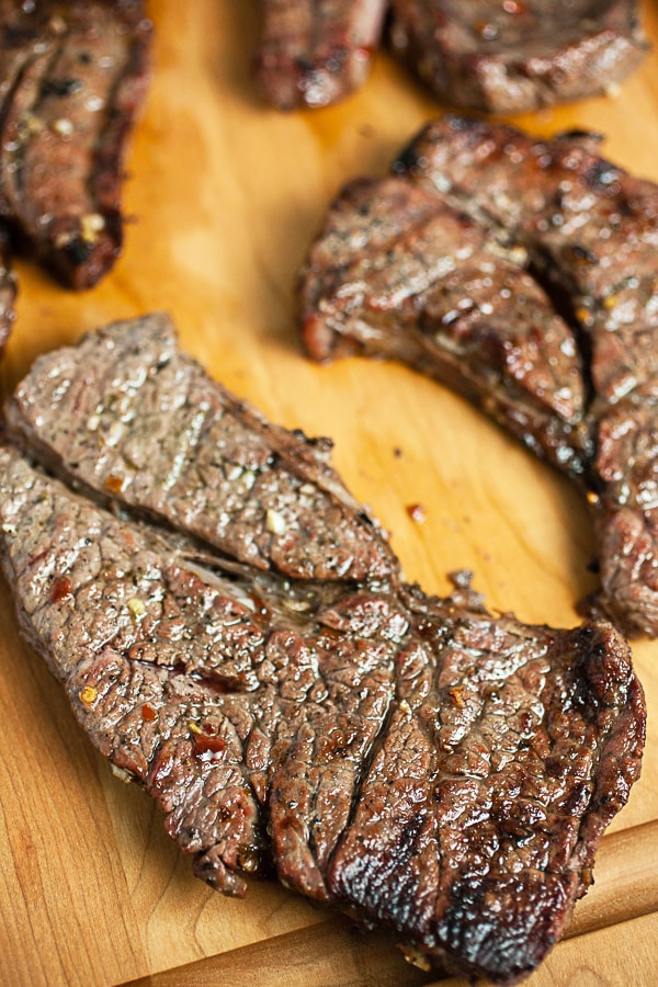 Grilled chuck steaks on wooden cutting board.