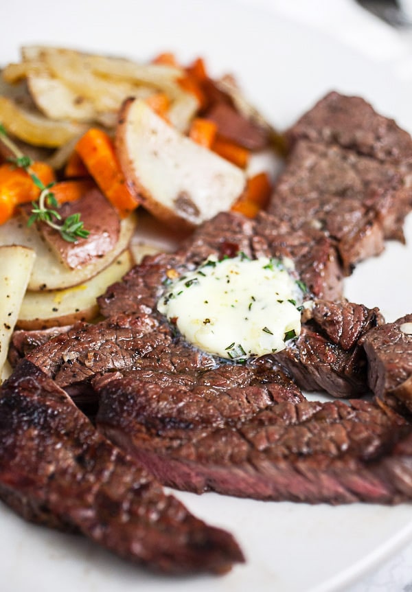 Grilled chuck steak with compound butter on white plate with potatoes and carrots.