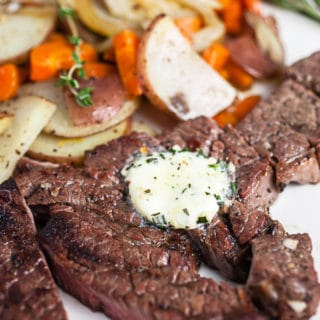 Grilled chuck steak topped with compound butter on white plate with potatoes and carrots.