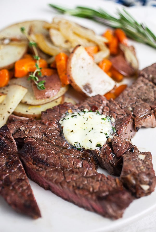 Grilled chuck steak topped with compound butter on white plate with potatoes and carrots.