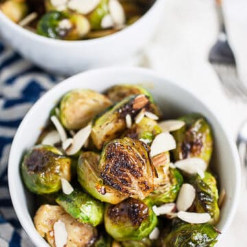 Roasted Brussels sprouts garnished with almonds in small white bowls.