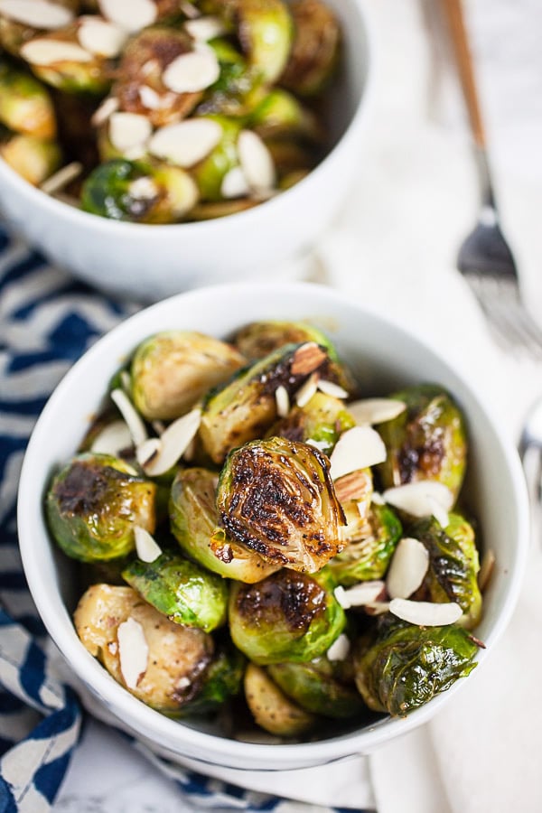 Roasted Brussels sprouts garnished with almonds in small white bowls.