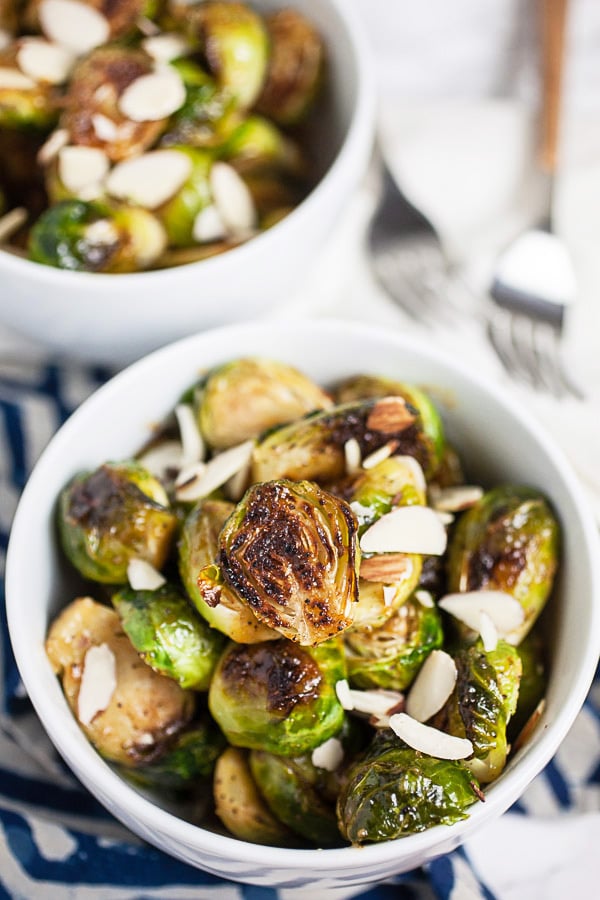Roasted Brussels sprouts with sliced almonds in small white bowls.