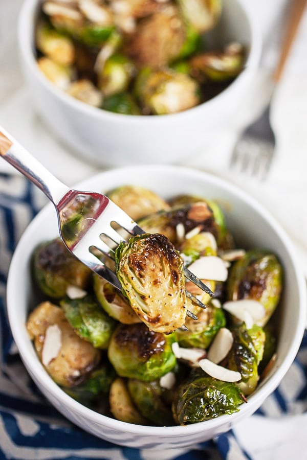 Fork holding Brussels sprouts lifted from small white bowl.