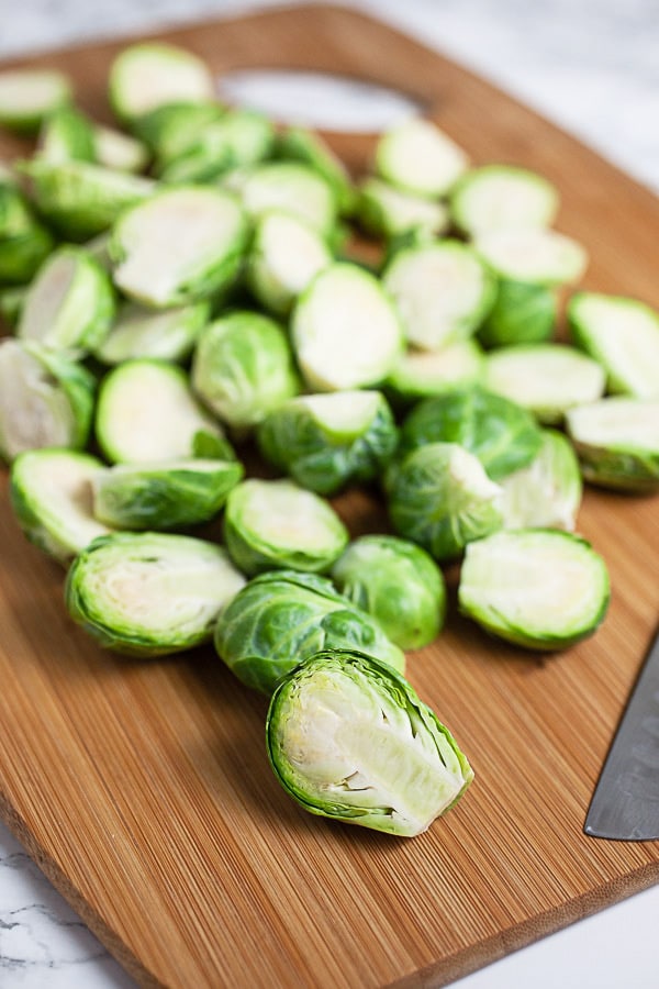 Chopped Brussels sprouts on wooden cutting board with knife.