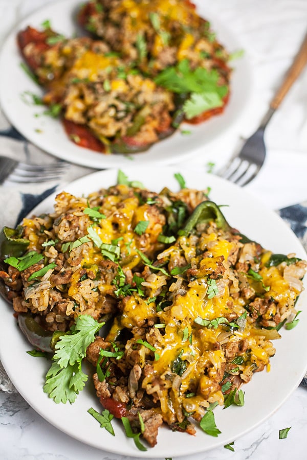 Stuffed poblano peppers with turkey, rice, melted cheese, and cilantro on small white plates.