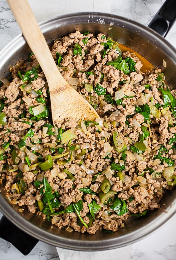 Garlic, onions, peppers, ground turkey, and spices sautéed in skillet with wooden spoon.