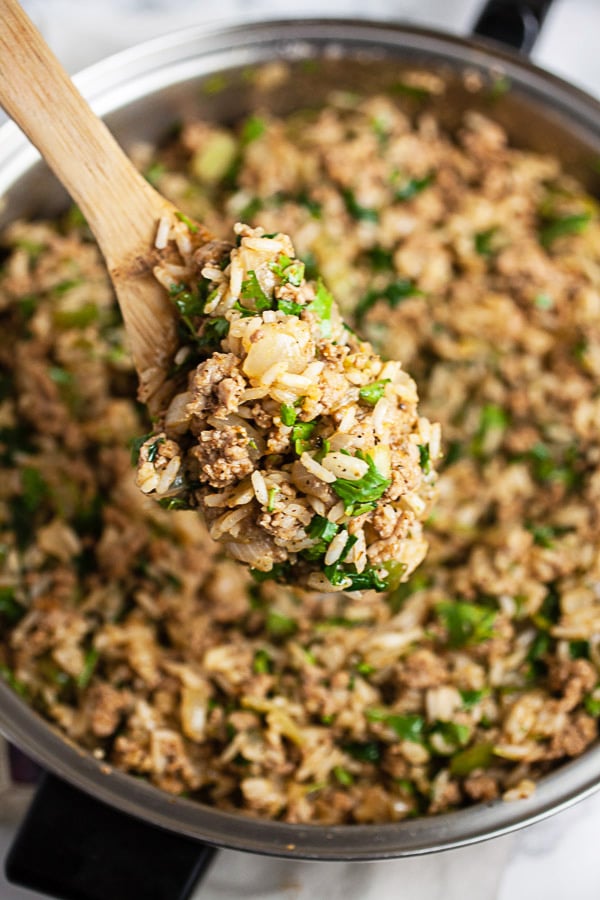 Wooden spoonful of ground turkey rice filling lifted from skillet.